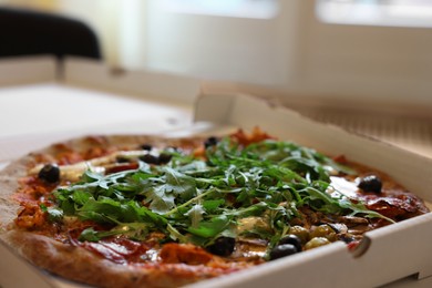 Delicious pizza with arugula, mushrooms and olives in box indoors, closeup