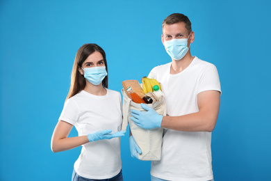 Photo of Volunteers in protective masks and gloves with products on blue background. Aid during coronavirus quarantine
