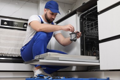 Photo of Repairman holding drain filter near dishwasher in kitchen, low angle view