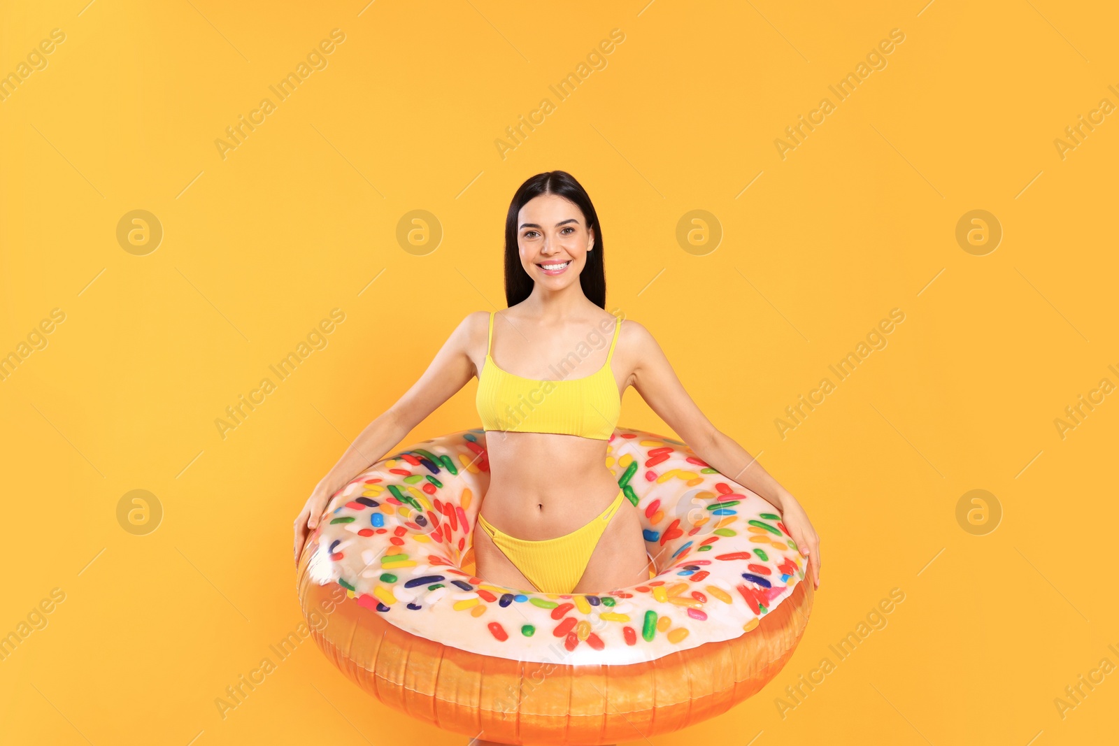 Photo of Happy young woman with beautiful suntan and inflatable ring against orange background