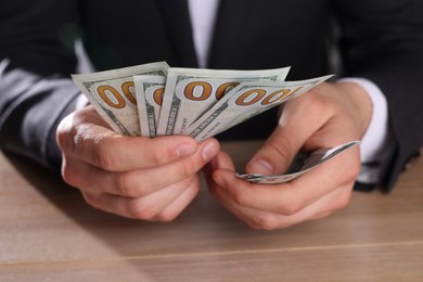 Photo of Money exchange. Man counting dollar banknotes at wooden table, closeup