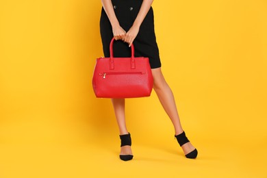 Woman with stylish bag on yellow background, closeup