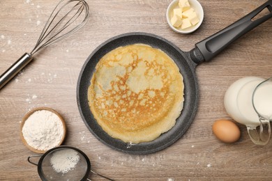 Frying pan with delicious crepe and ingredients on wooden table, flat lay