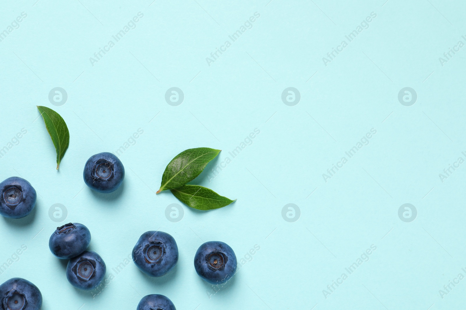 Photo of Tasty fresh blueberries with green leaves on light blue background, flat lay. Space for text