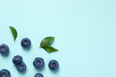 Tasty fresh blueberries with green leaves on light blue background, flat lay. Space for text