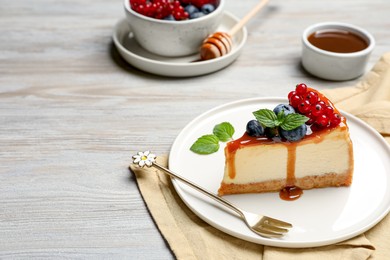 Slice of delicious cheesecake served with berries and caramel sauce on white wooden table, space for text