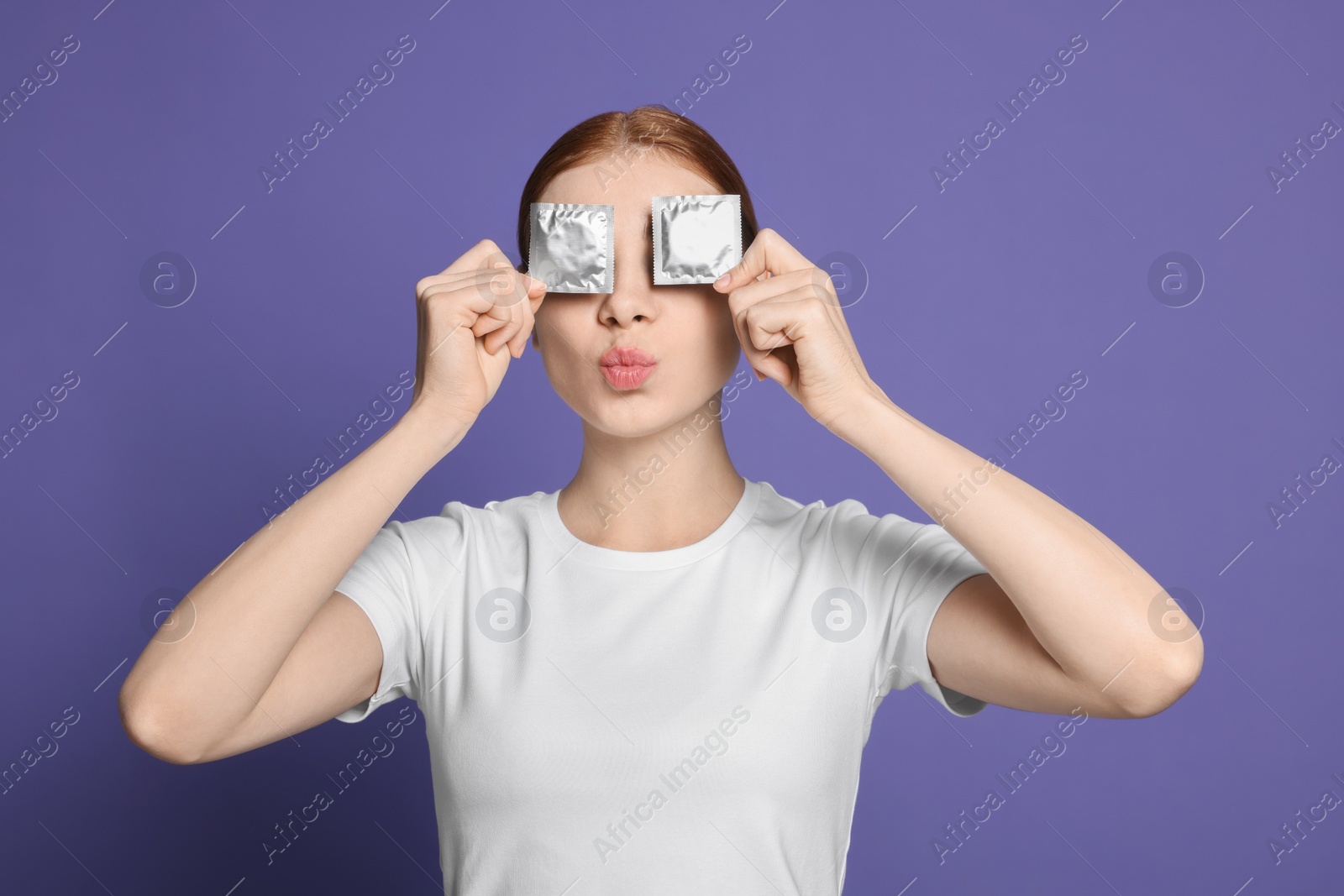 Photo of Woman holding condoms near her eyes on purple background. Safe sex