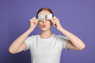 Photo of Woman holding condoms near her eyes on purple background. Safe sex
