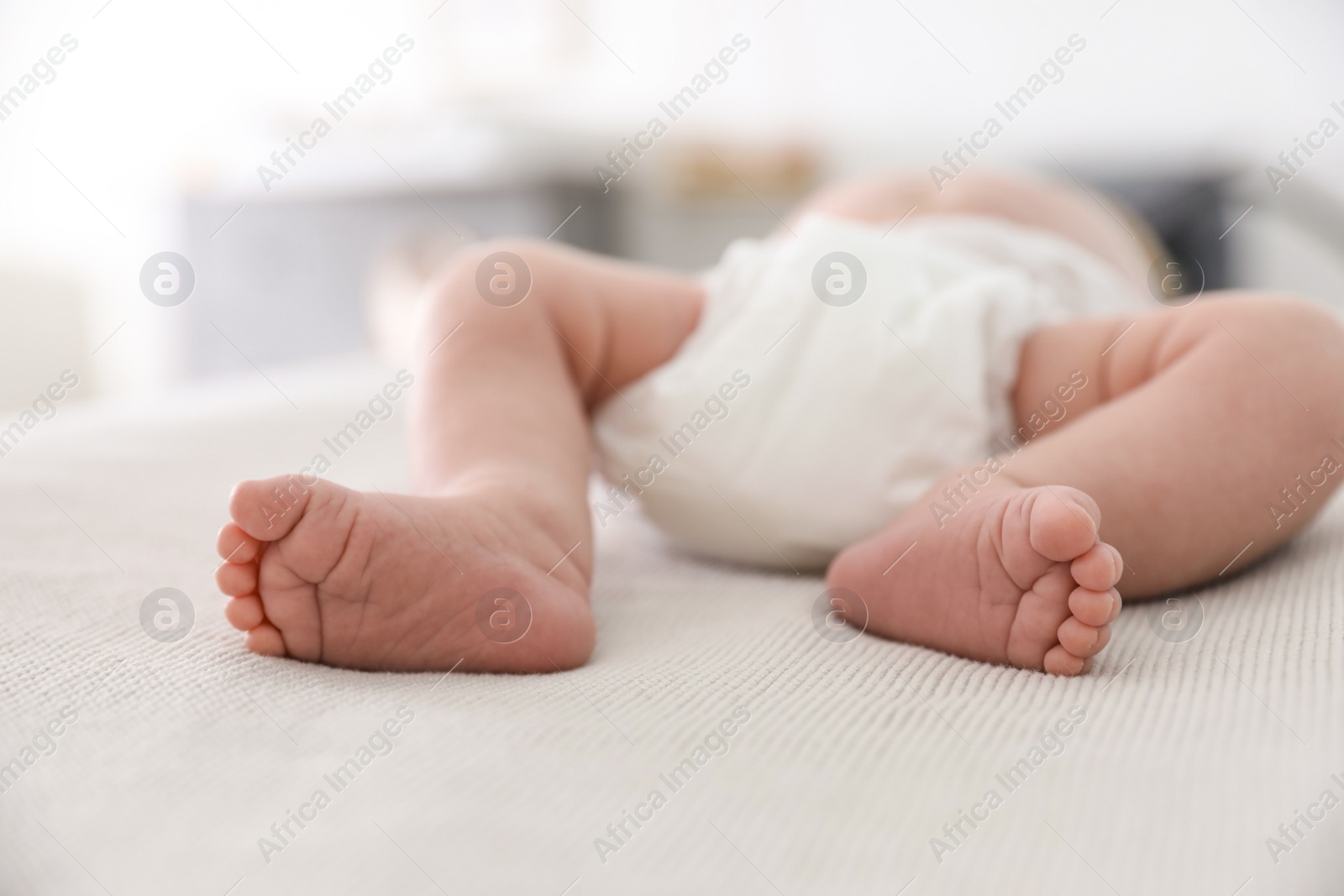 Photo of Cute little baby in diaper lying on bed in room, closeup