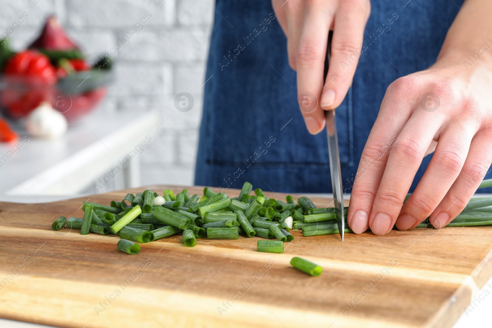 Photo of Woman cutting green spring onion on wooden board, closeup