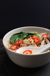 Photo of Bowl of vegetarian ramen and spoon on dark wooden table, closeup