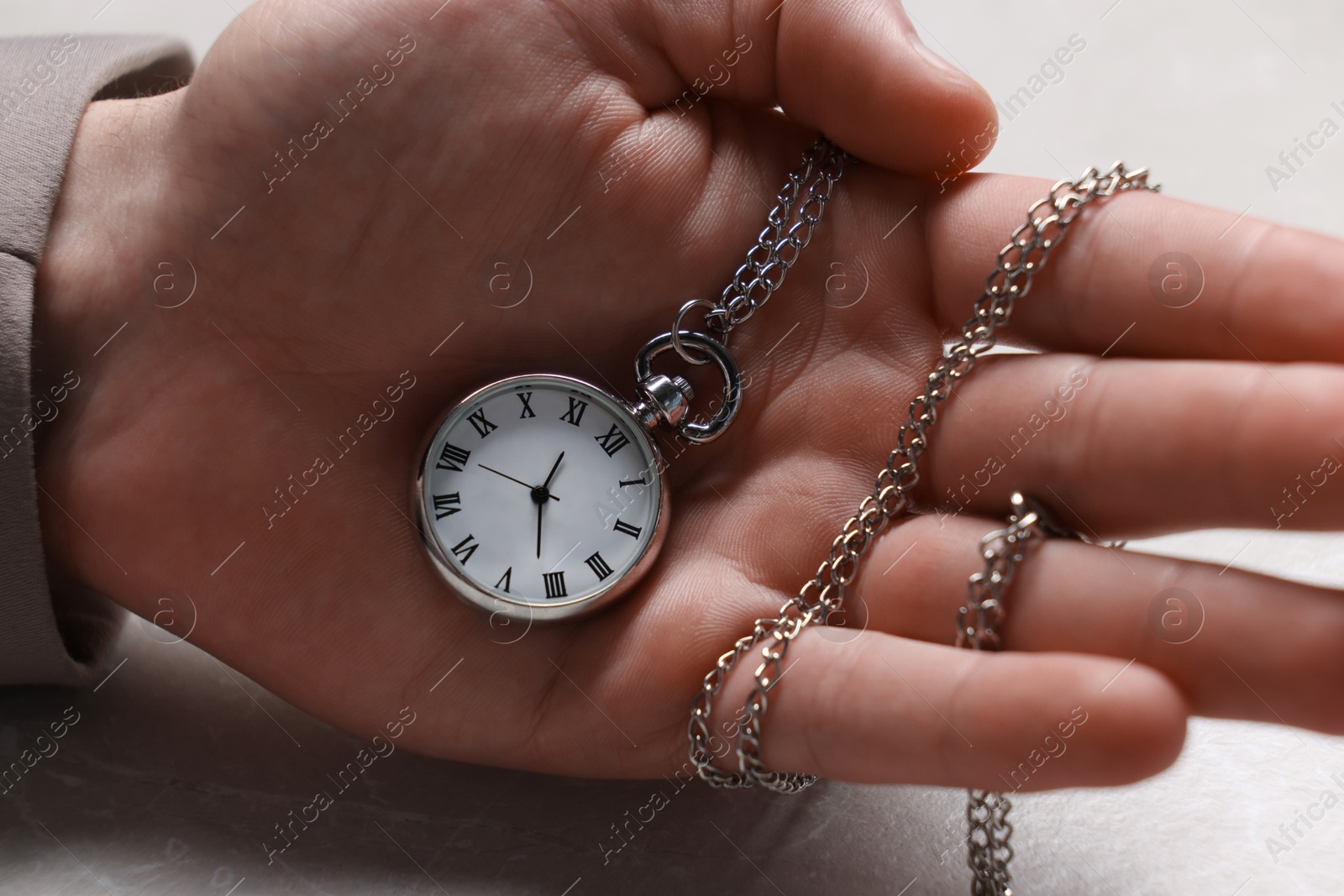 Photo of Man holding chain with elegant pocket watch at light textured table, closeup