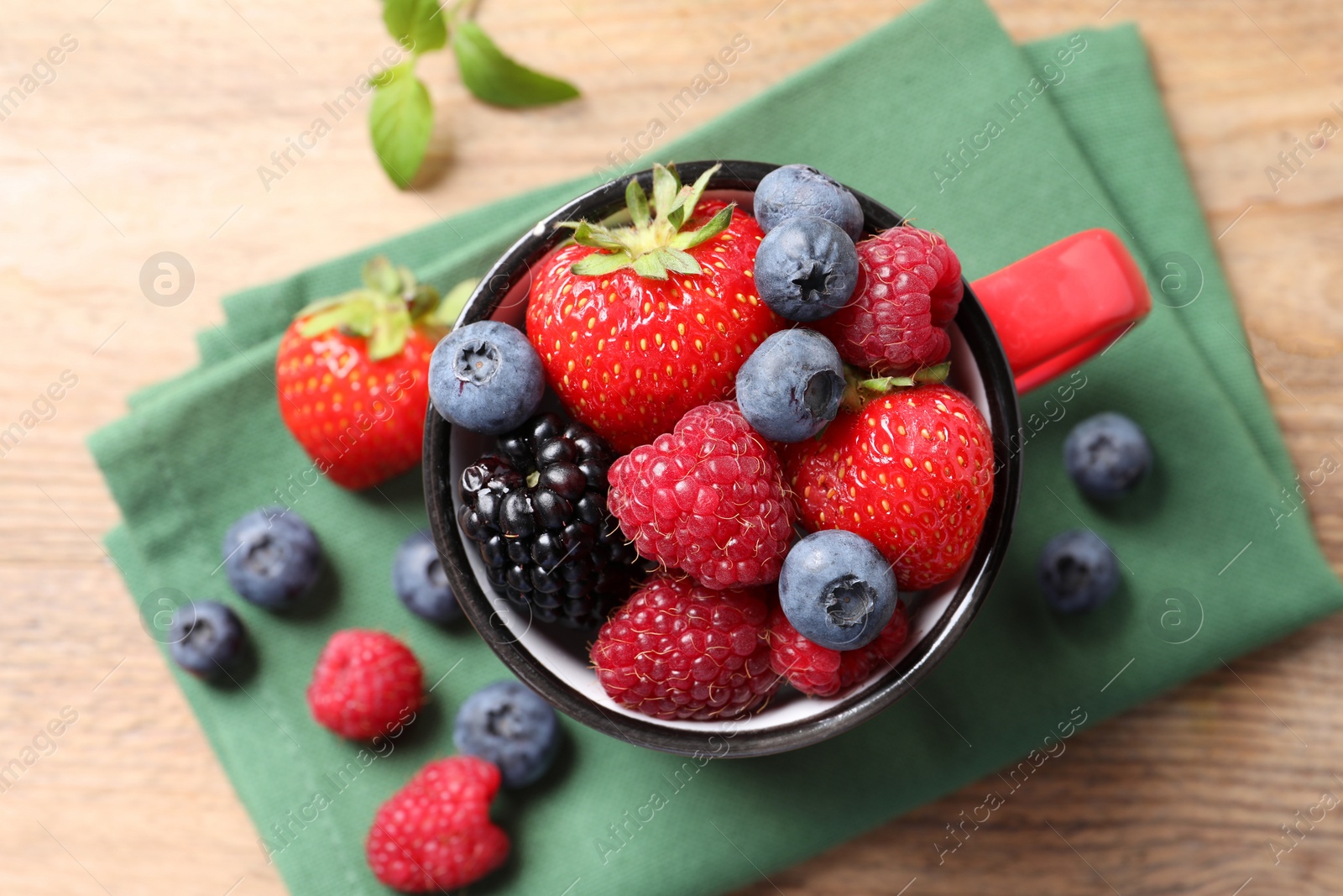 Photo of Many different fresh ripe berries in mug on wooden table, top view