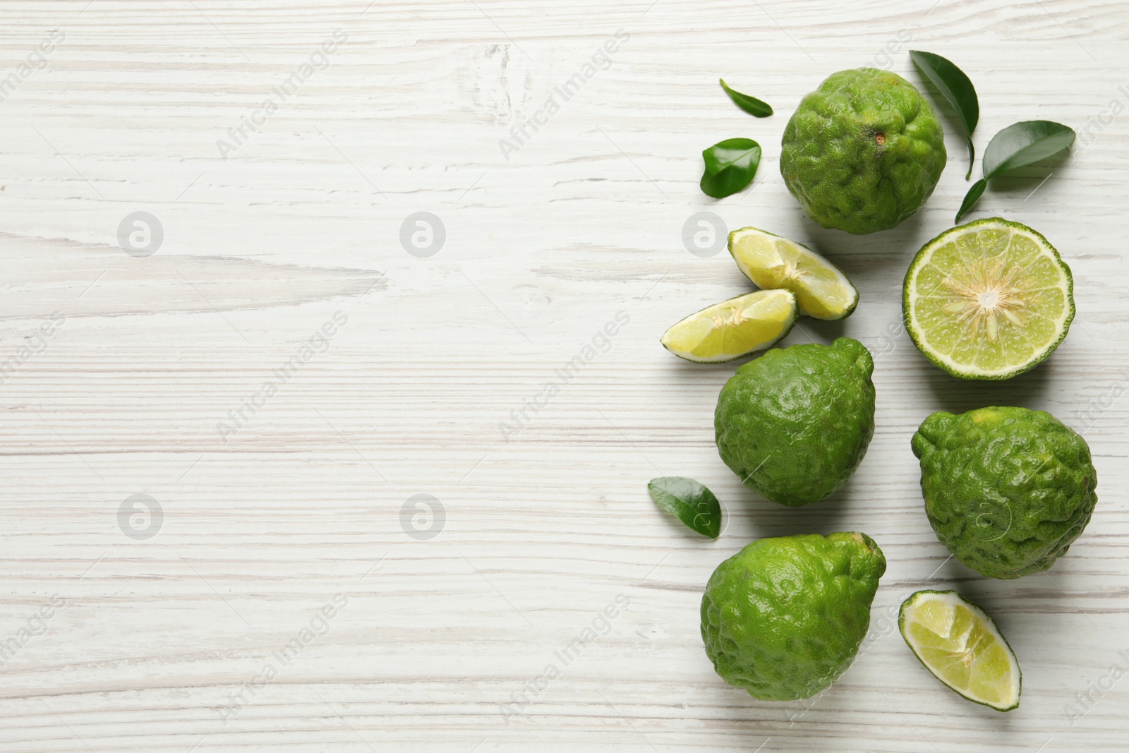 Photo of Fresh ripe bergamot fruits with green leaves on white wooden table, flat lay. Space for text