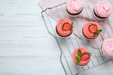 Photo of Delicious cupcakes with cream and strawberries on white wooden table, top view. Space for text