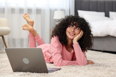 Beautiful young woman in stylish pyjama with laptop on floor at home