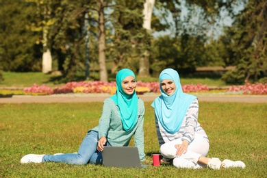 Photo of Muslim women in hijabs with laptop sitting on green lawn outdoors