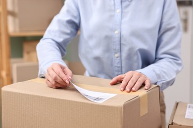 Parcel packing. Post office worker sticking barcode on box indoors, closeup