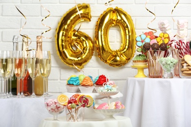 Dessert table in room decorated with golden balloons for 60 year birthday party