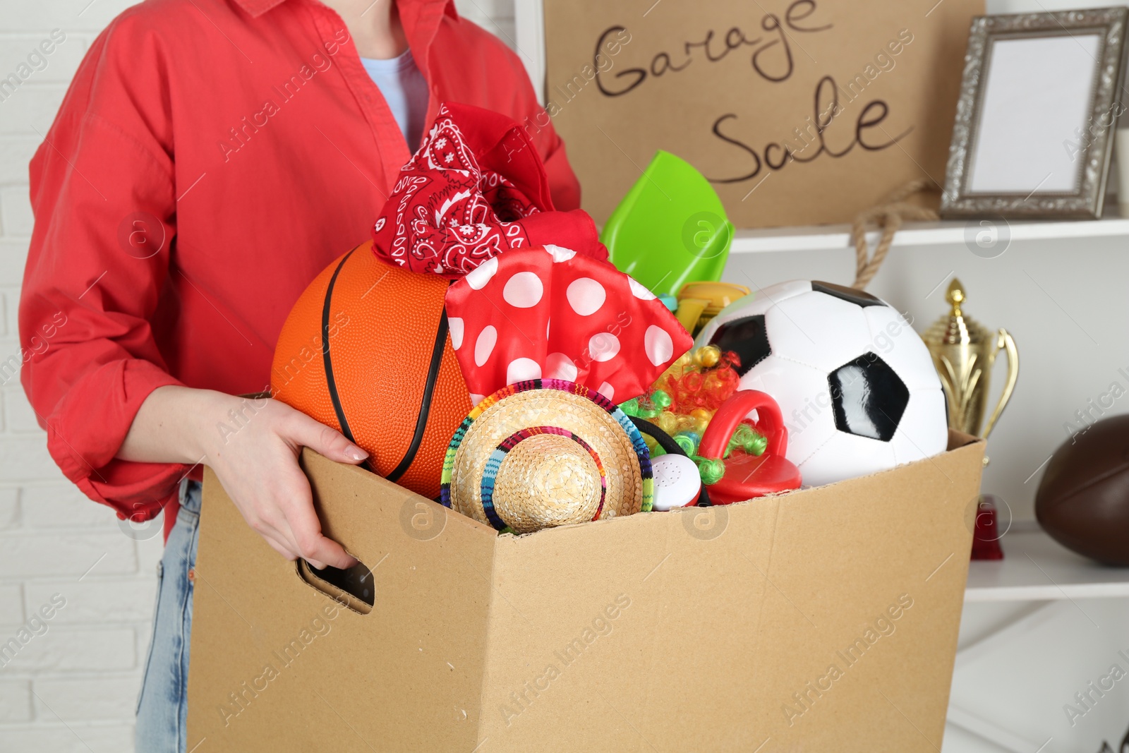 Photo of Woman holding box of unwanted stuff indoors, closeup