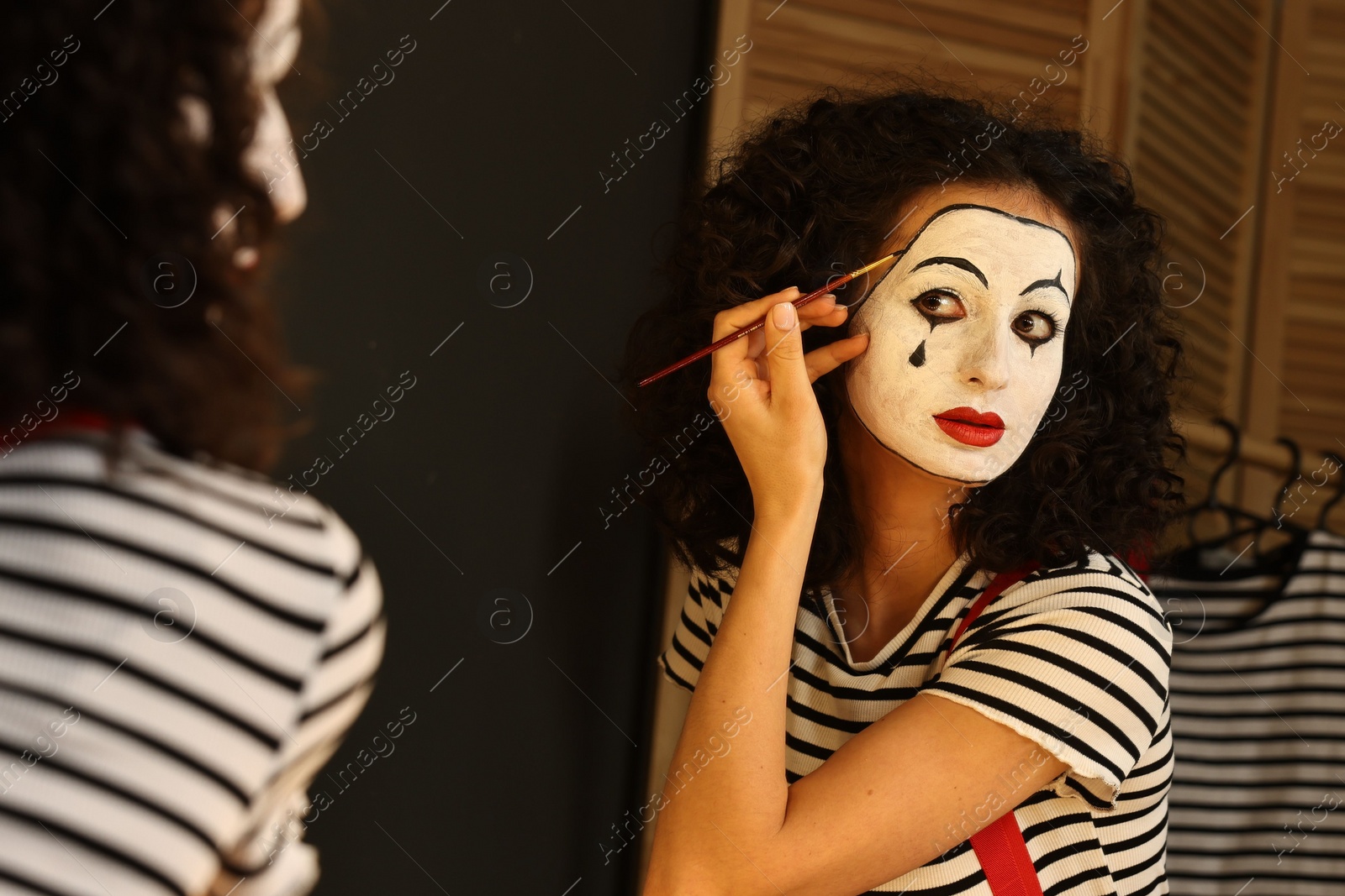 Photo of Young woman applying mime makeup near mirror indoors