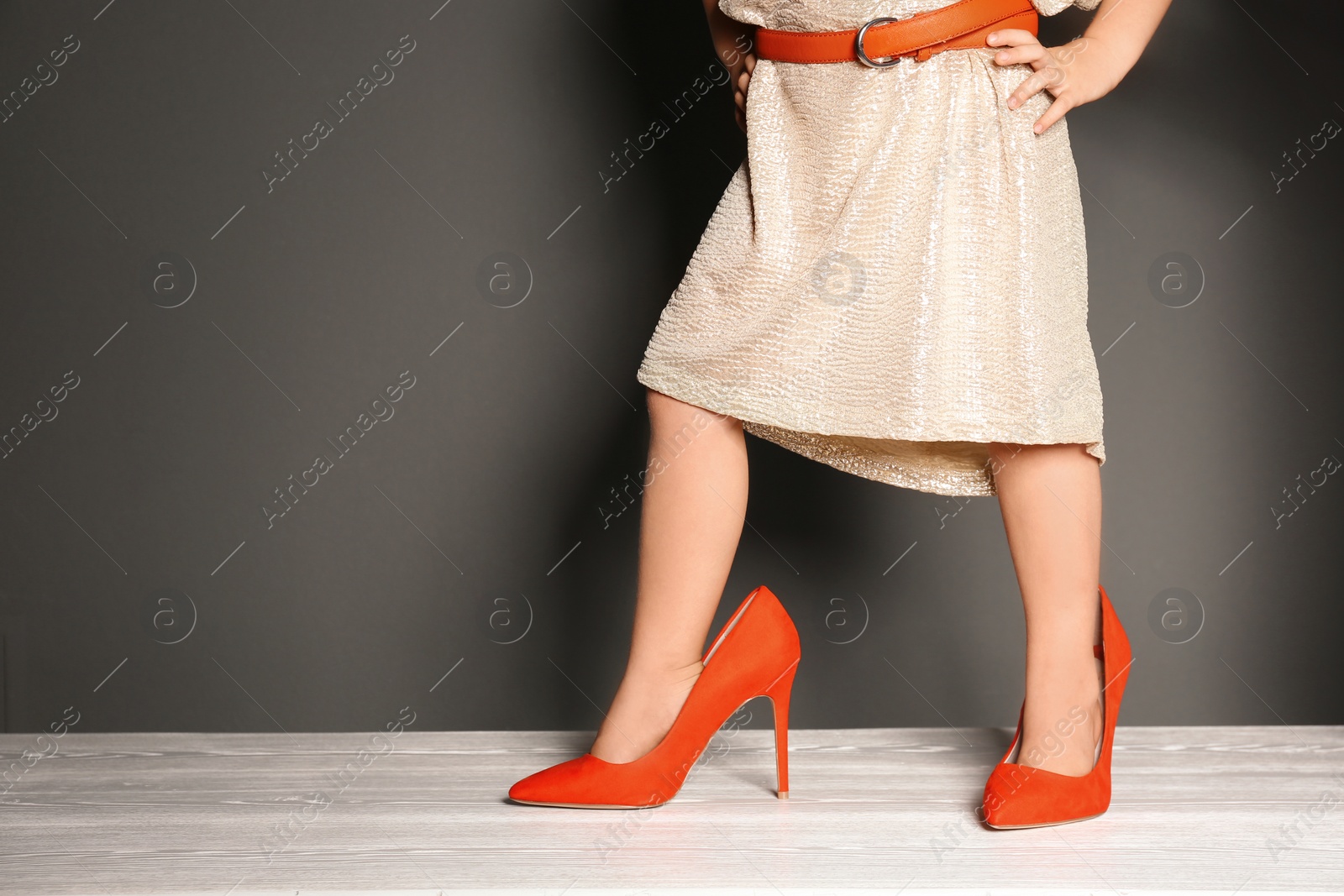 Photo of Little girl in oversized shoes near black wall with space for text, closeup on legs