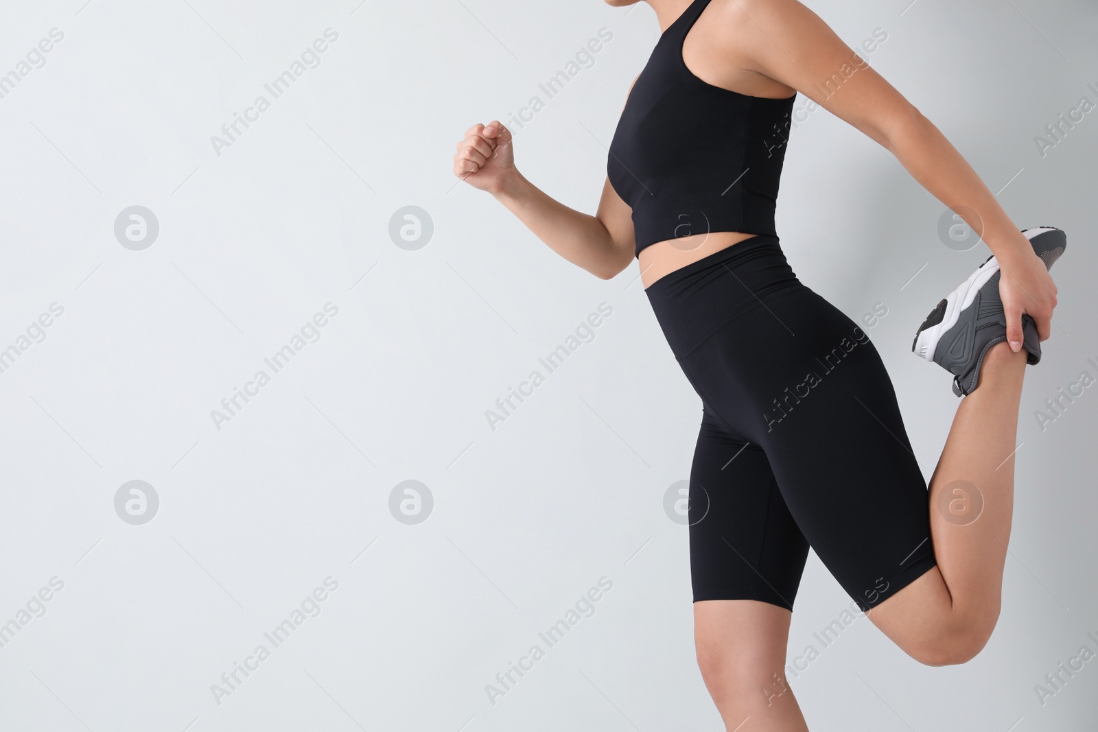 Photo of Young woman wearing black sportive clothes near light wall, closeup. Space for text