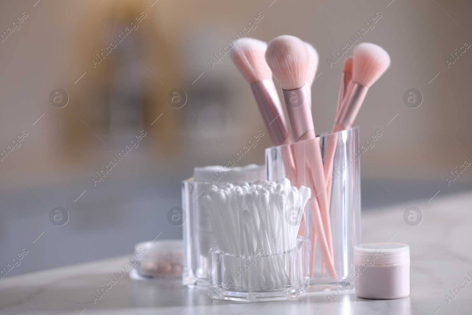 Photo of Cotton buds, pads and makeup brushes in transparent holders on light table