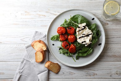 Photo of Delicious burrata cheese served with tomatoes, croutons, arugula and basil on white wooden table, flat lay