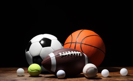 Photo of Many different sport balls on wooden table against black background