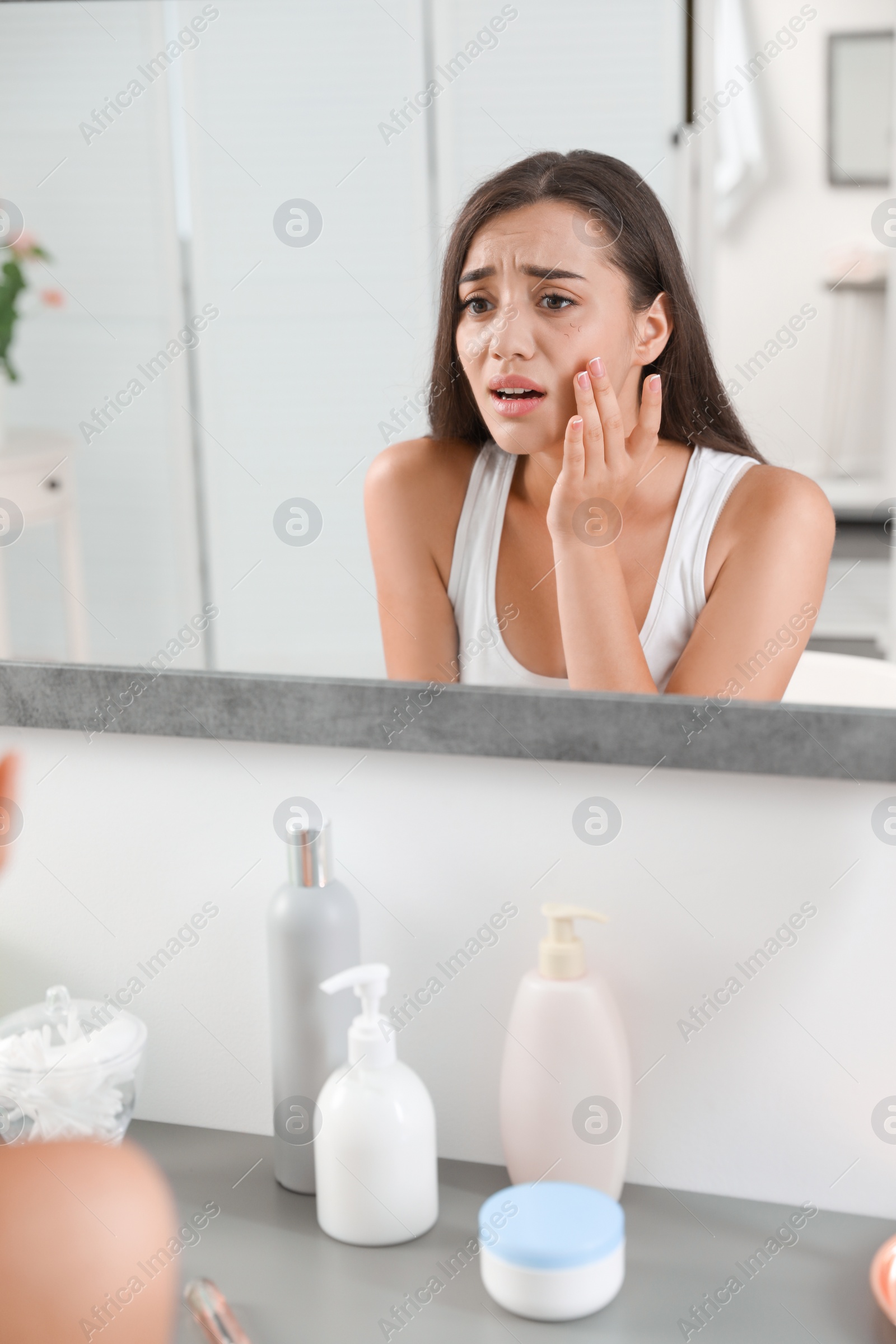 Photo of Young woman with eyelash loss problem looking in mirror indoors