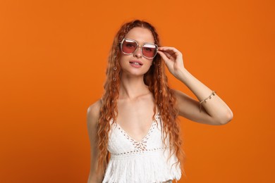 Photo of Stylish young hippie woman in sunglasses on orange background