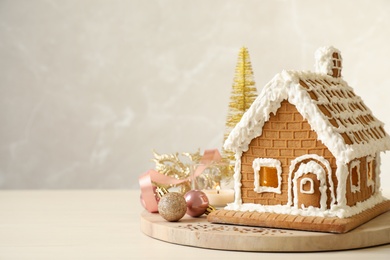 Beautiful gingerbread house decorated with icing and Christmas balls on table, space for text