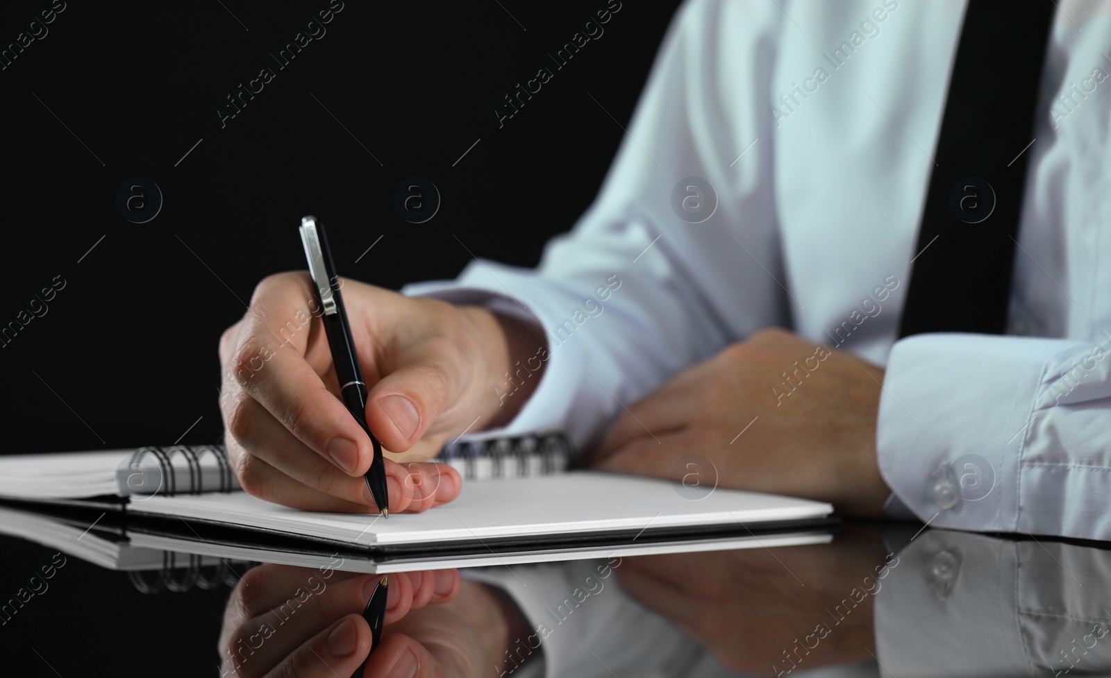 Photo of Man writing in notebook at black table, closeup