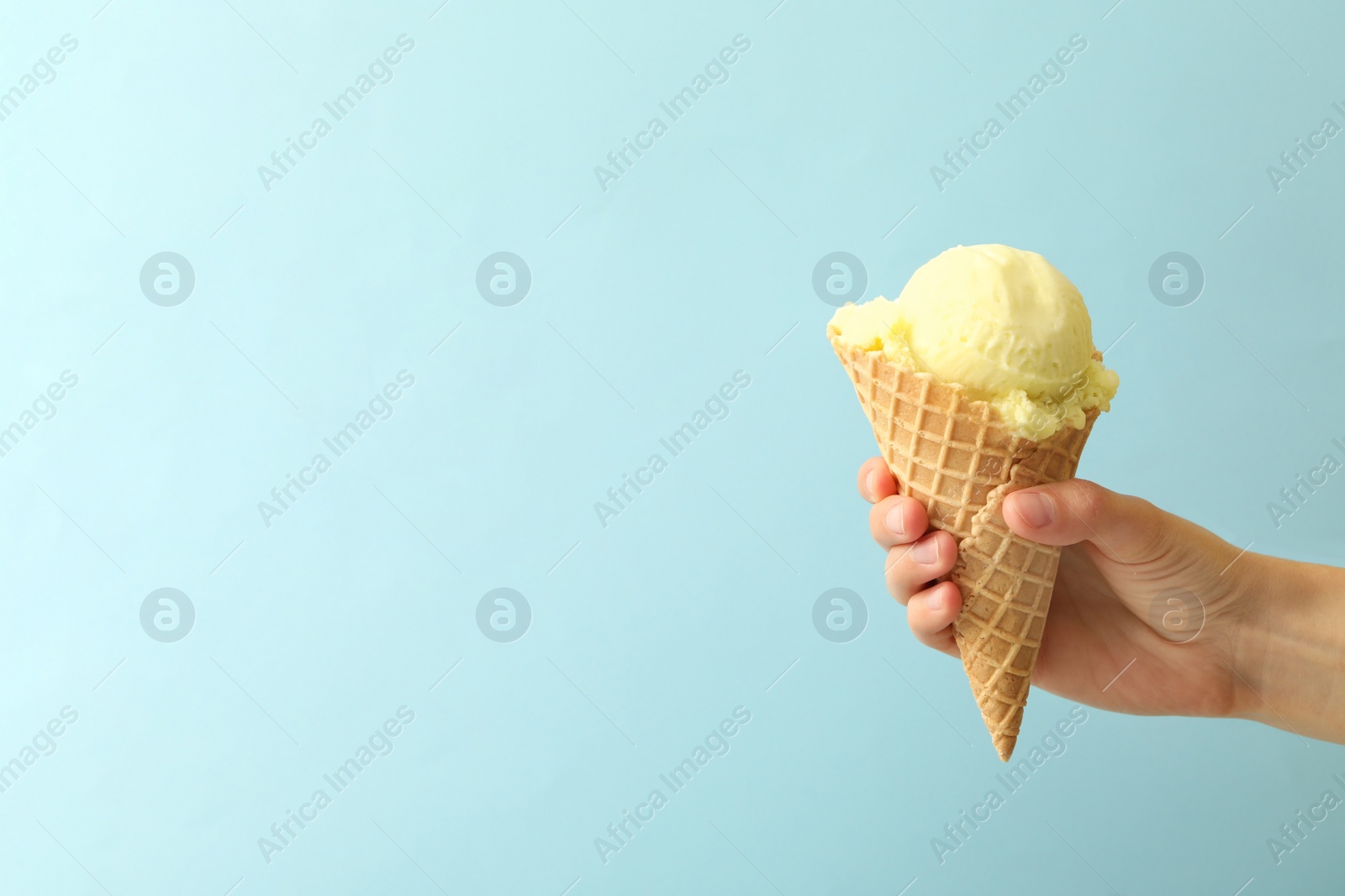 Photo of Woman holding waffle cone with delicious yellow ice cream on light blue background, closeup. Space for text