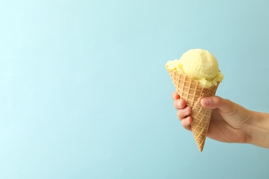 Woman holding waffle cone with delicious yellow ice cream on light blue background, closeup. Space for text