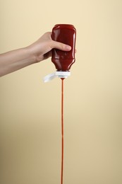 Woman pouring tasty ketchup from bottle on beige background, closeup