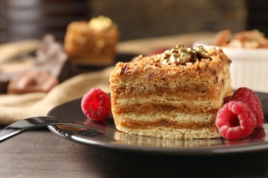 Photo of Pieces of delicious layered honey cake with nuts and raspberries on wooden table, closeup