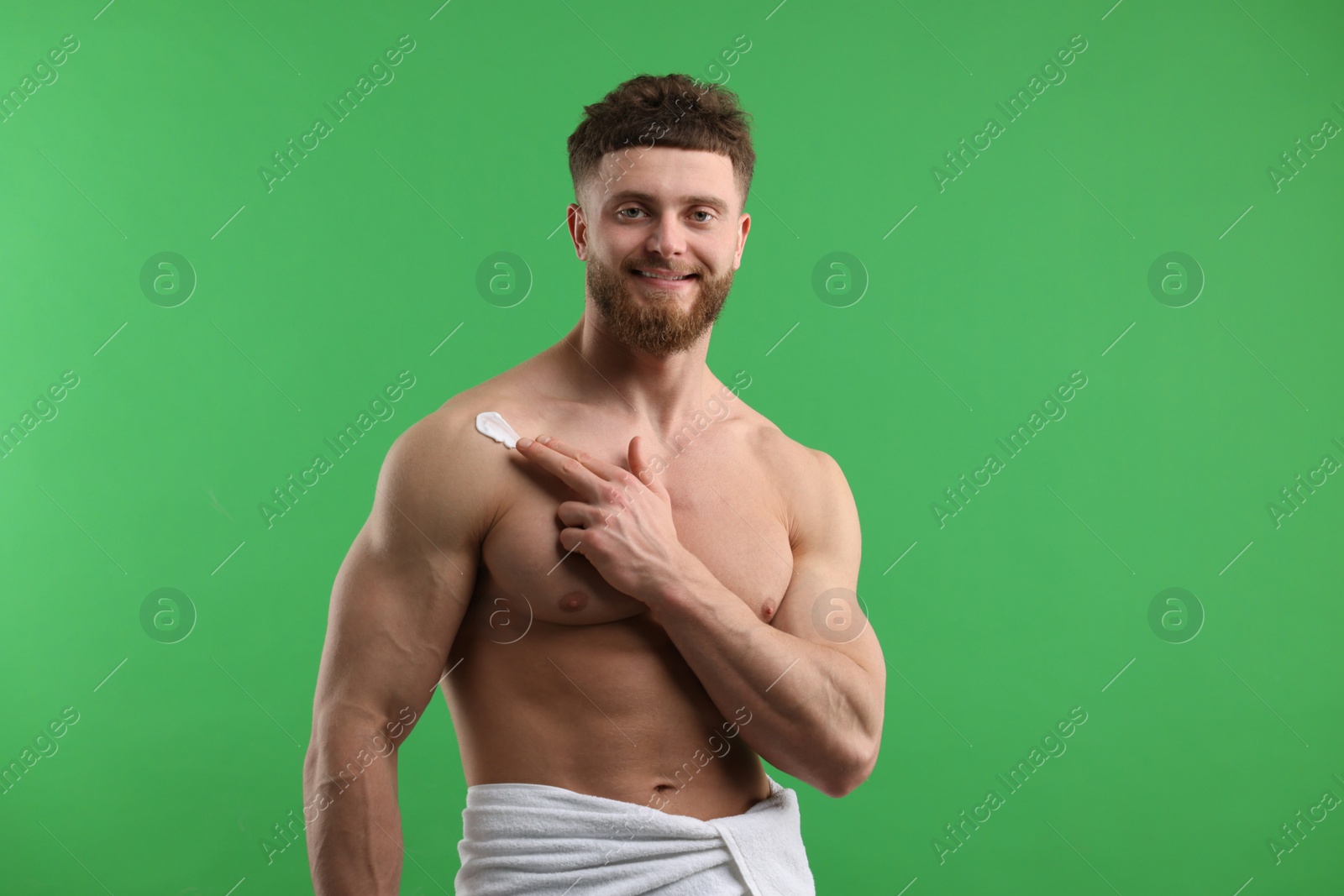 Photo of Handsome man applying moisturizing cream onto his shoulder on green background