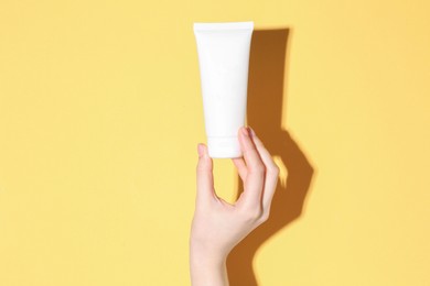 Woman holding tube of cream on yellow background, closeup