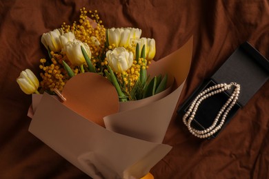 Bouquet of beautiful spring flowers, blank card and necklace on brown fabric, flat lay