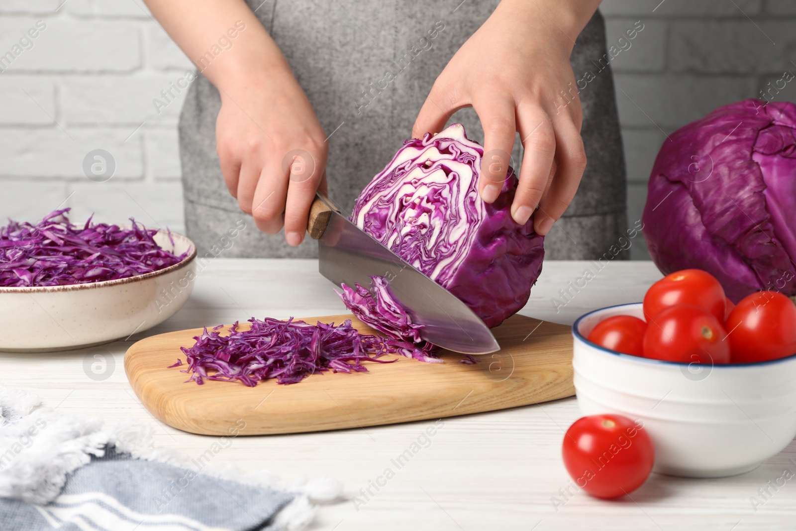 Photo of Woman cutting fresh red cabbage at white wooden table, closeup