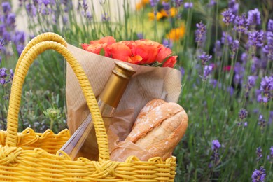 Yellow wicker bag with beautiful roses, bottle of wine and baguettes in garden, closeup