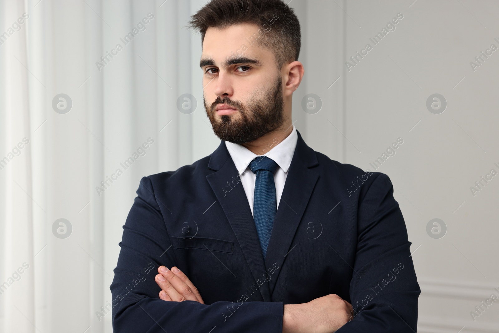 Photo of Handsome businessman in suit and necktie with crossed arms indoors