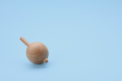 Photo of One wooden spinning top on light blue background, space for text. Toy whirligig