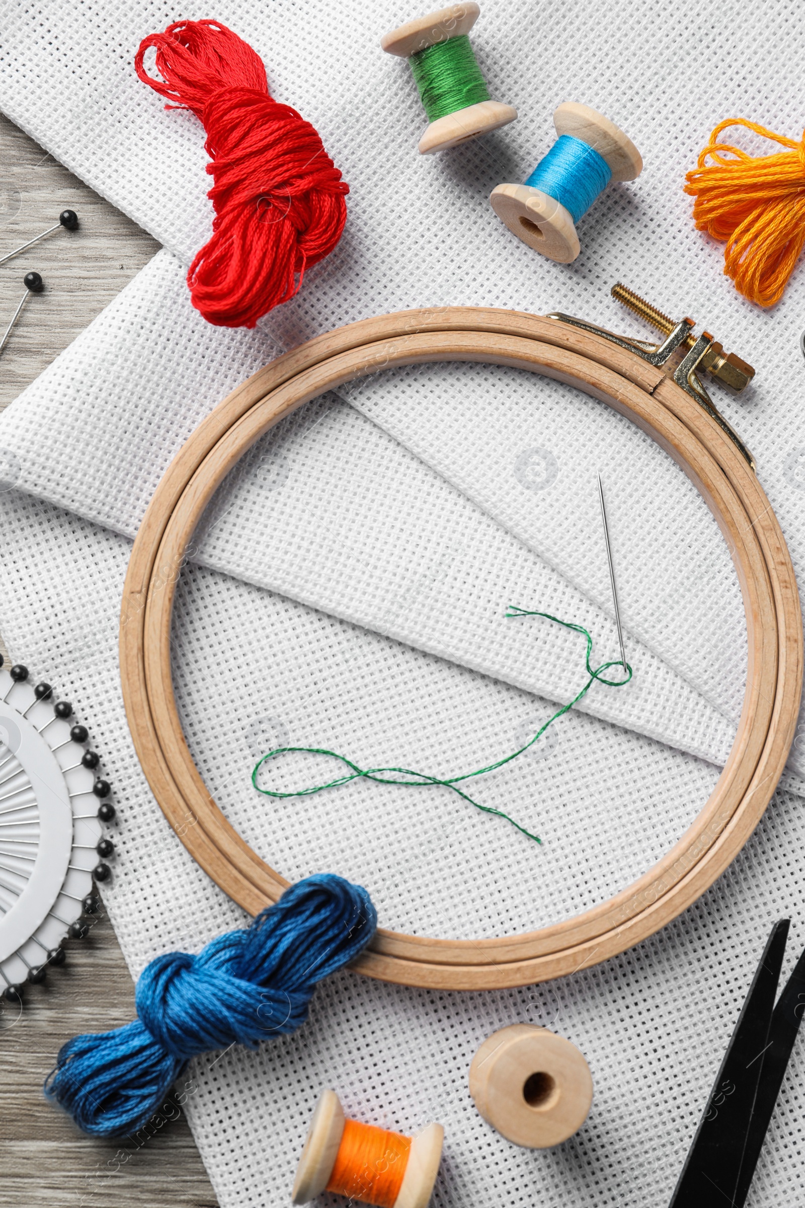 Photo of Embroidery hoop, fabric and other accessories on wooden table, flat lay