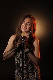 Photo of Beautiful young woman in stylish dress with microphone singing on dark background