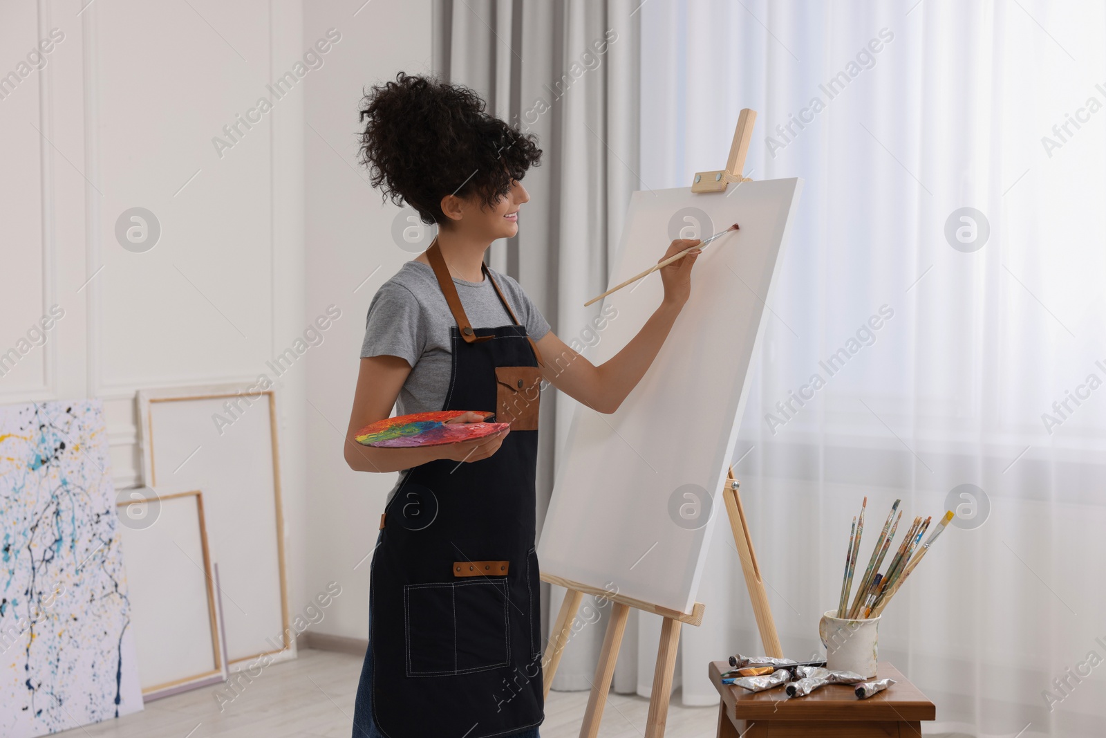 Photo of Young woman painting on easel with canvas in studio