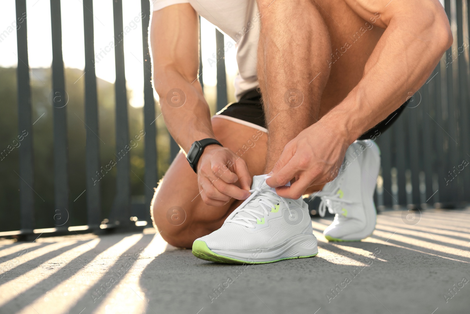 Photo of Man tying shoelaces before running outdoors on sunny day, closeup. Space for text