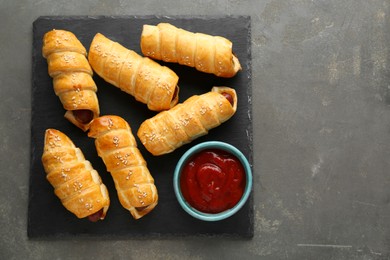 Delicious sausage rolls and ketchup on grey table, top view. Space for text